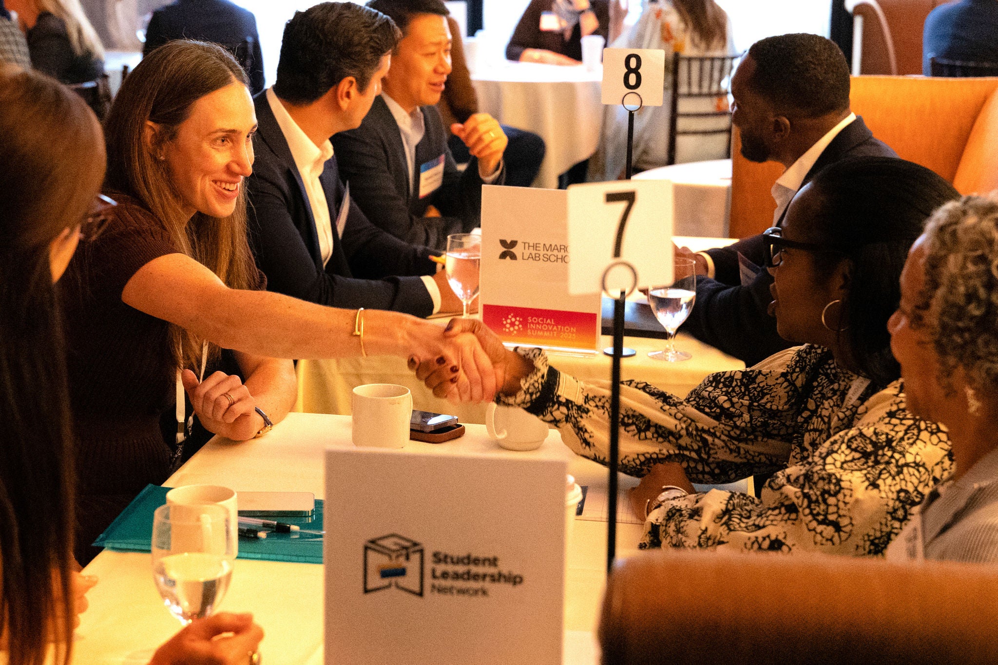Attendees at the Social Innovation Summit 2025 participate in nonprofit board matchmaking, exchanging handshakes and ideas across tables marked by nonprofit organization signs.