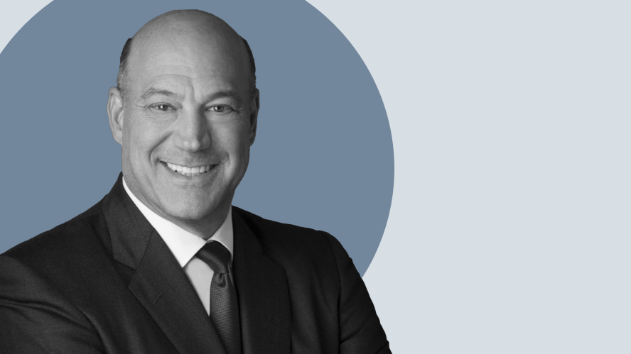 Portrait of Gary Cohn, bald man in a dark suit and tie, smiling with arms crossed in front of a muted blue and gray circular background.